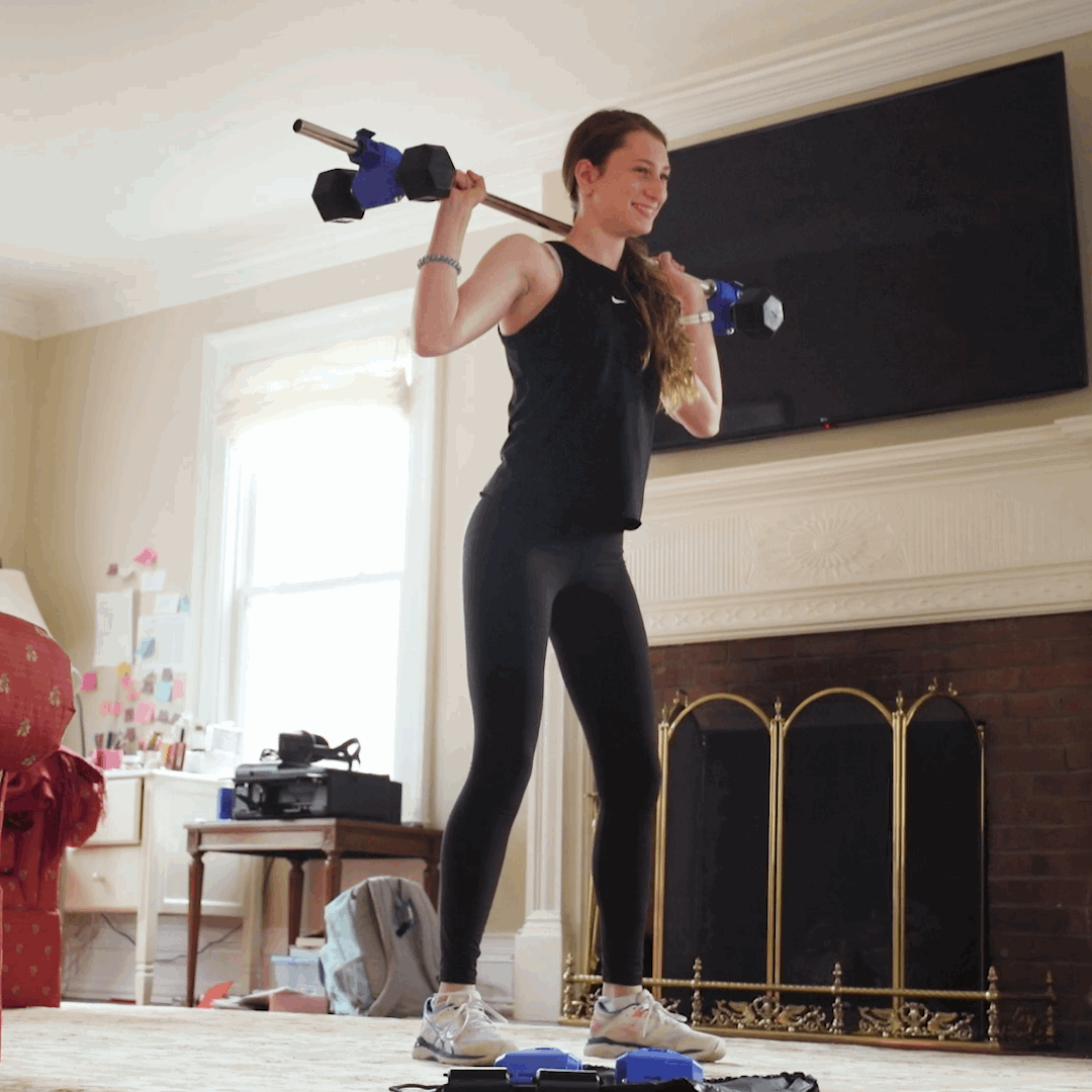 female doing barbell squat using dumbbells in place of weight plates on bar